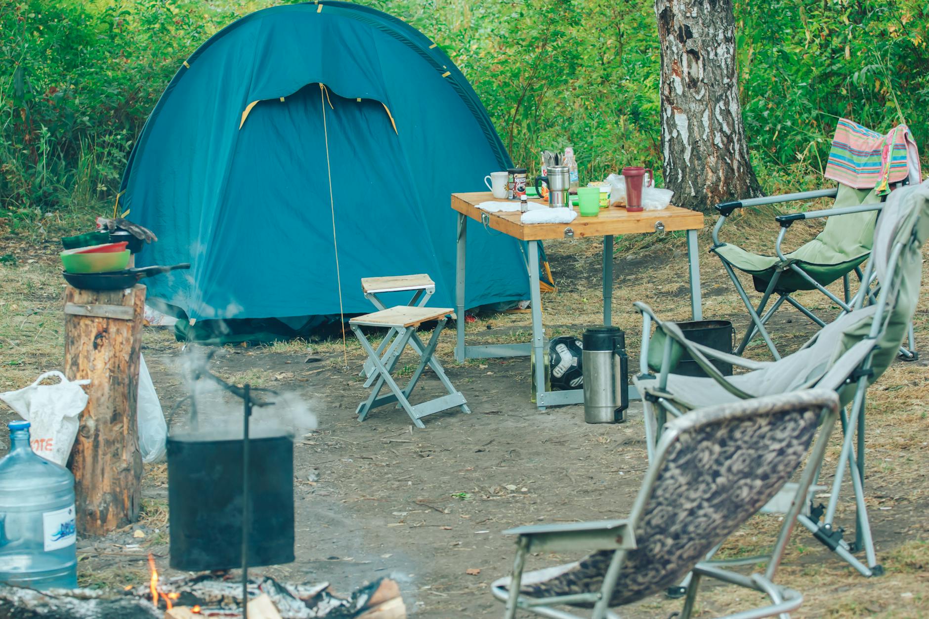 Serene campsite featuring a tent, chairs, and campfire amidst lush greenery for a perfect outdoor adventure.
