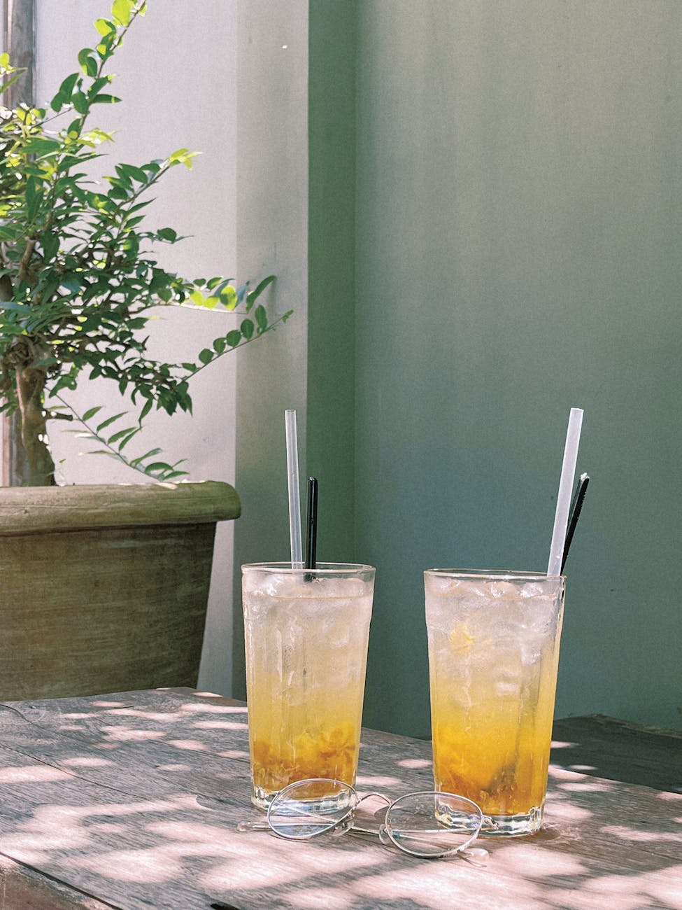 Two glasses of iced lemon tea on a wooden table in sunny outdoor setting.