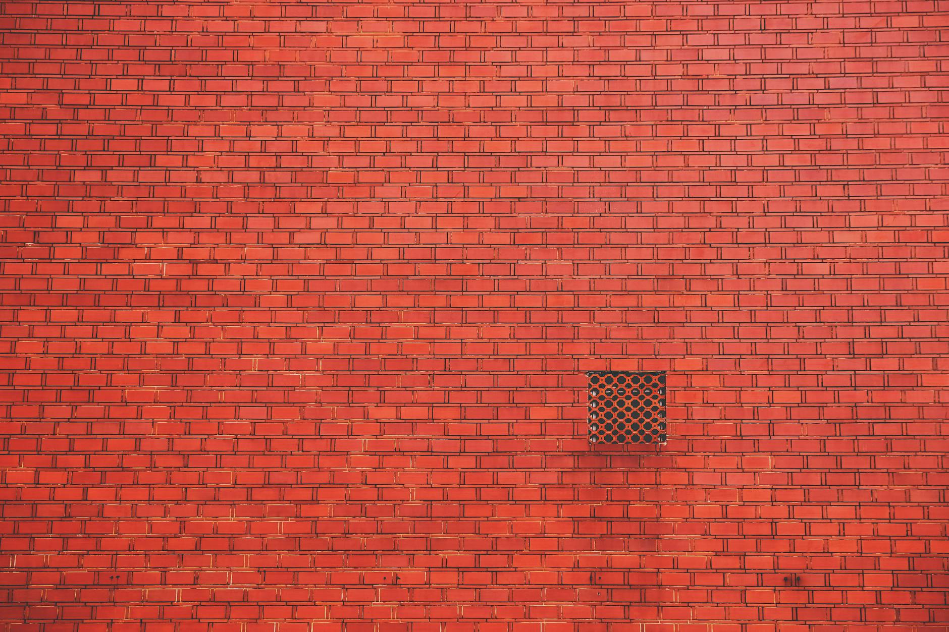 A vibrant red brick wall featuring a small geometric lattice window, perfect for architectural textures.