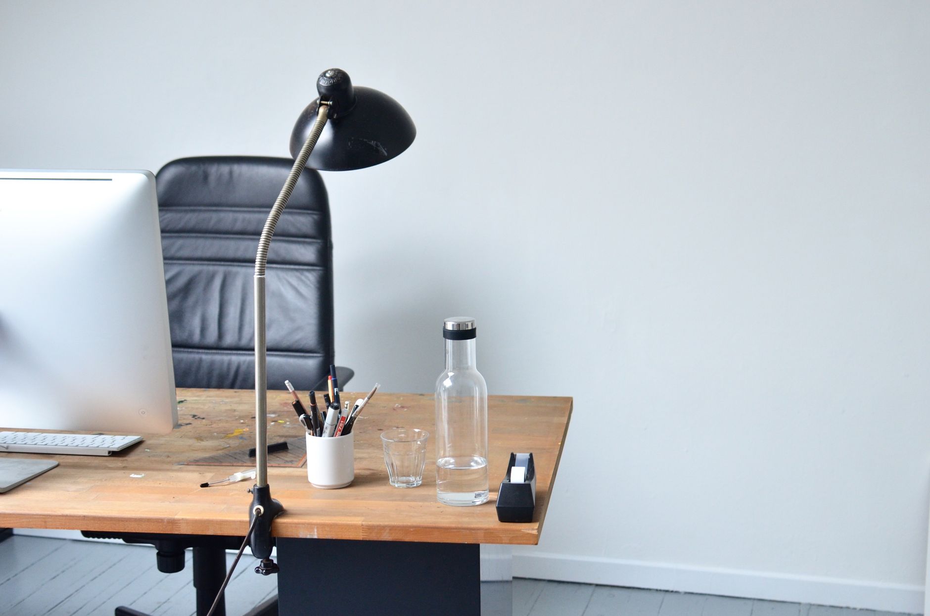 Modern minimalistic workplace with contemporary laptop placed on wooden table with bottle of water and lamp with big leather chair