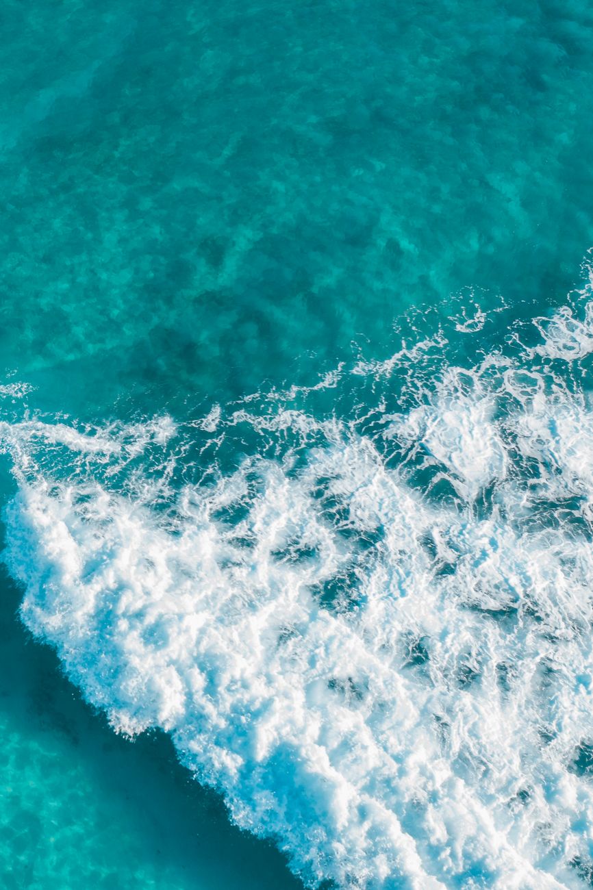 Stunning aerial view of turquoise ocean waves crashing onto the shore, captured from above.