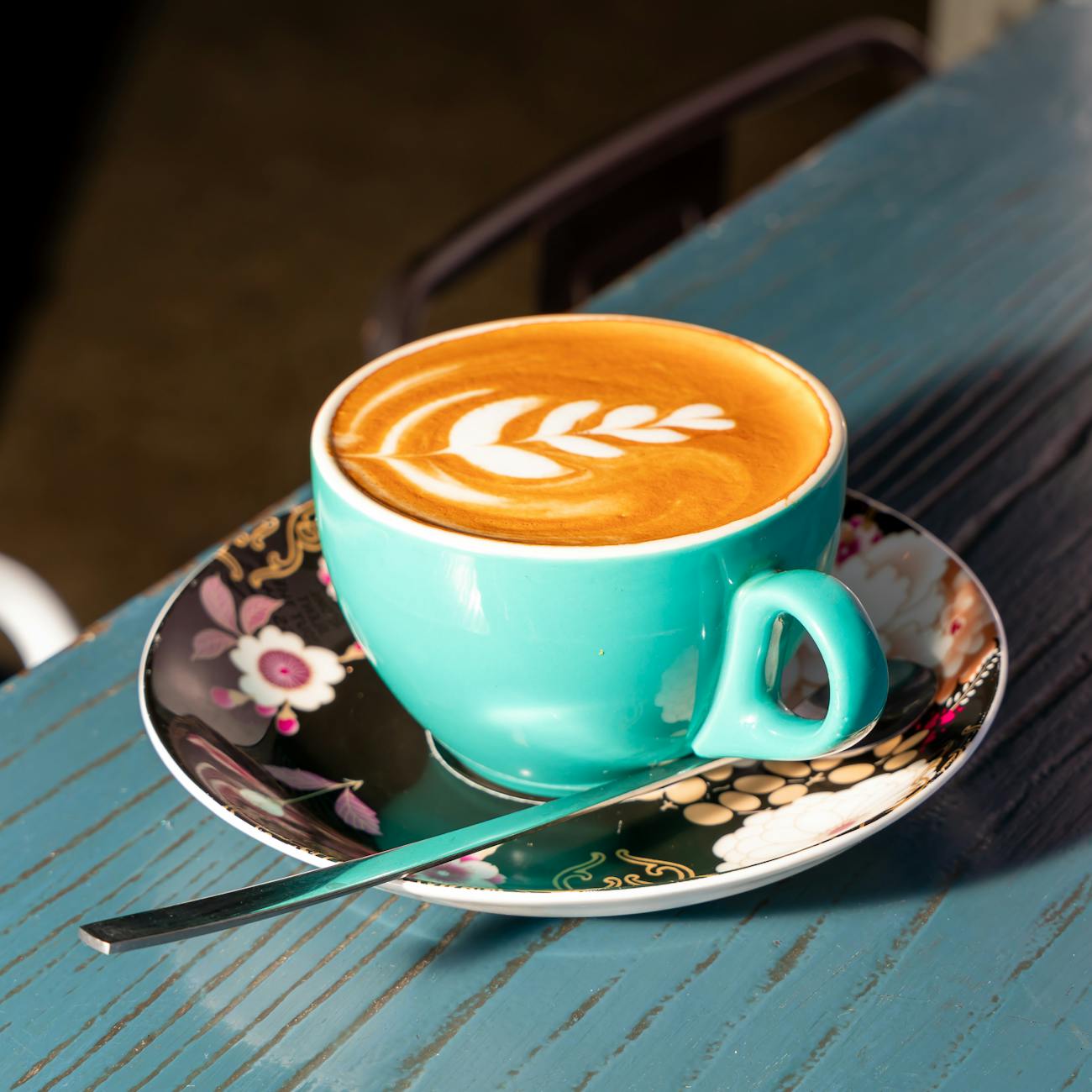 A close-up of a vibrant blue cup with elegant latte art on a patterned saucer.