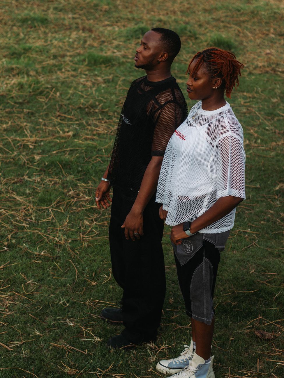 Stylish couple in mesh clothing standing on grass, showcasing modern fashion.