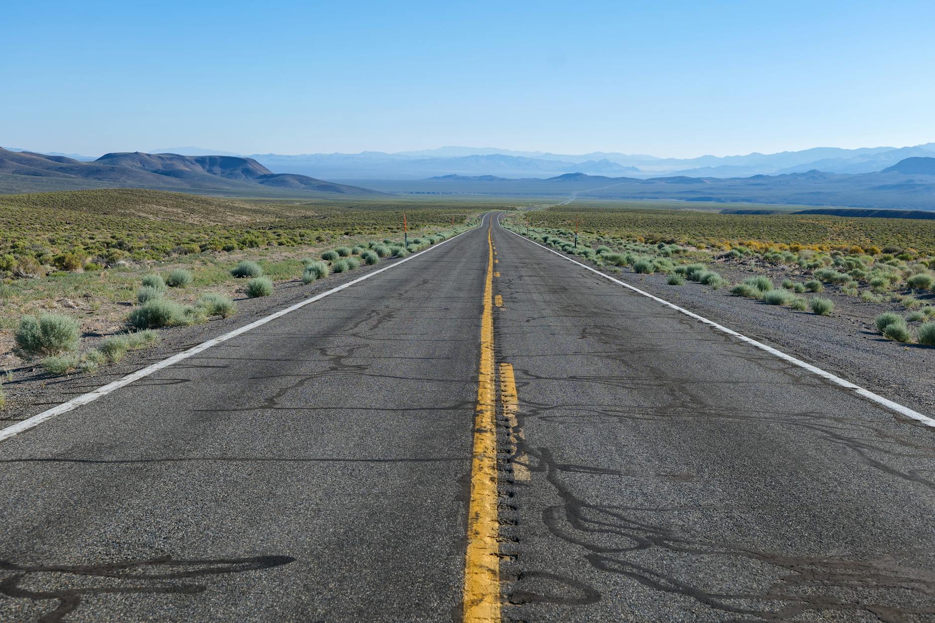 A long empty road stretches through a vast desert landscape under a clear blue sky.