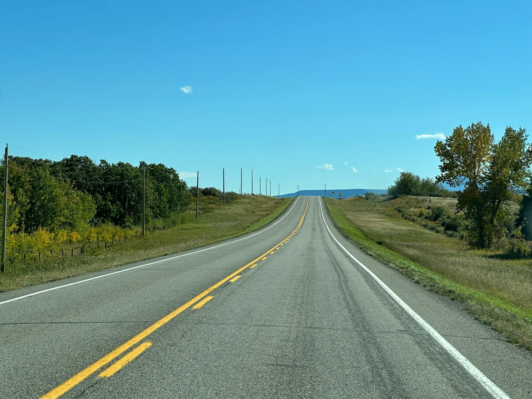 Empty highway under a clear blue sky with distant mountains visible on the horizon.