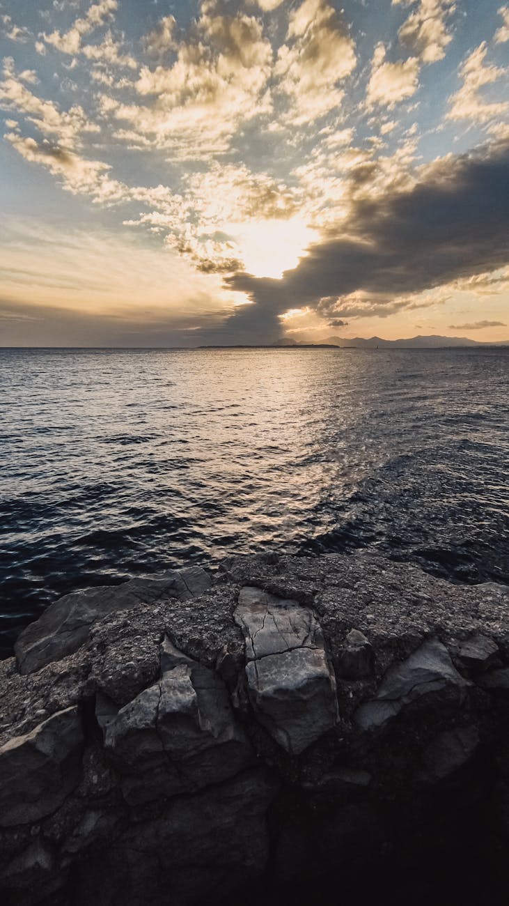 A stunning seascape featuring a sunset over the ocean with rocky foreground and vibrant clouds in the sky.