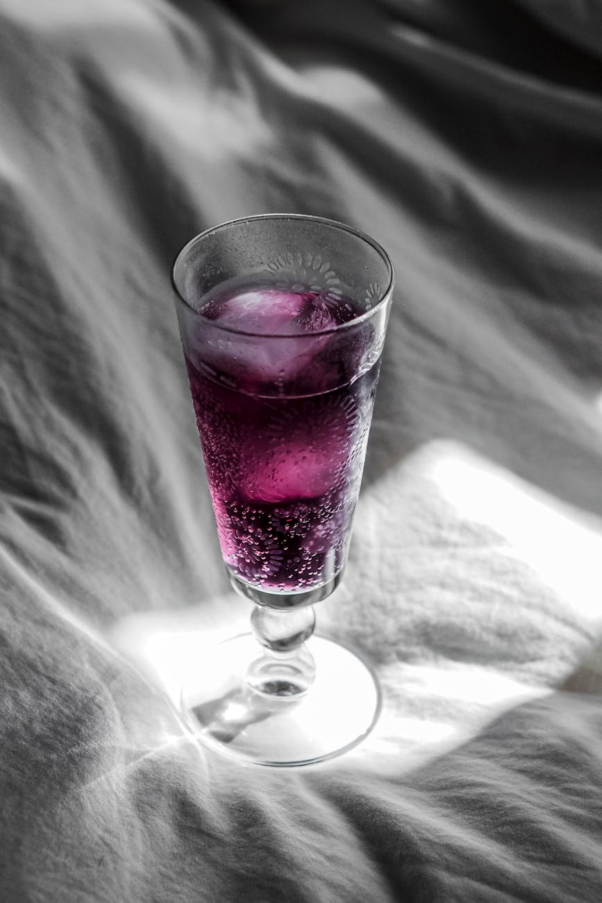 A close-up of a purple fizzy drink in an elegant glass on a fabric background.
