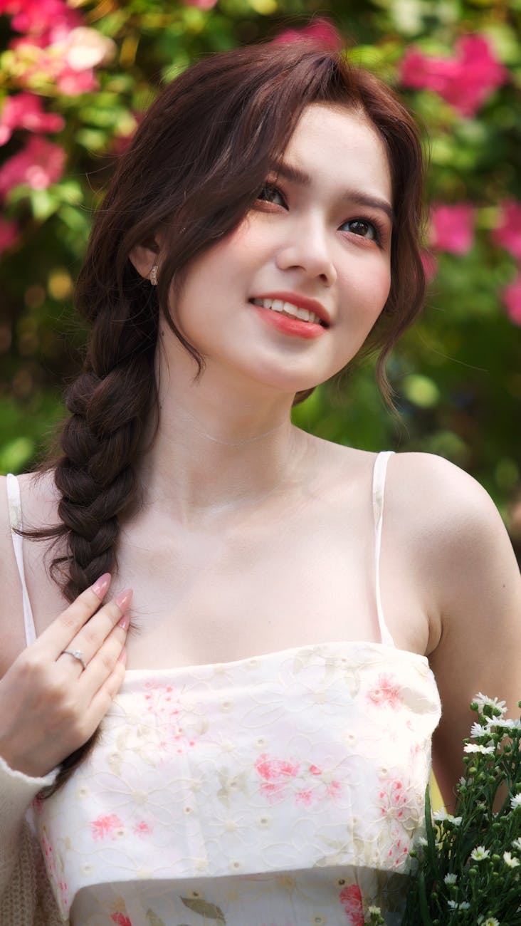 Smiling woman with braided hair surrounded by vibrant flowers in a sunny garden.