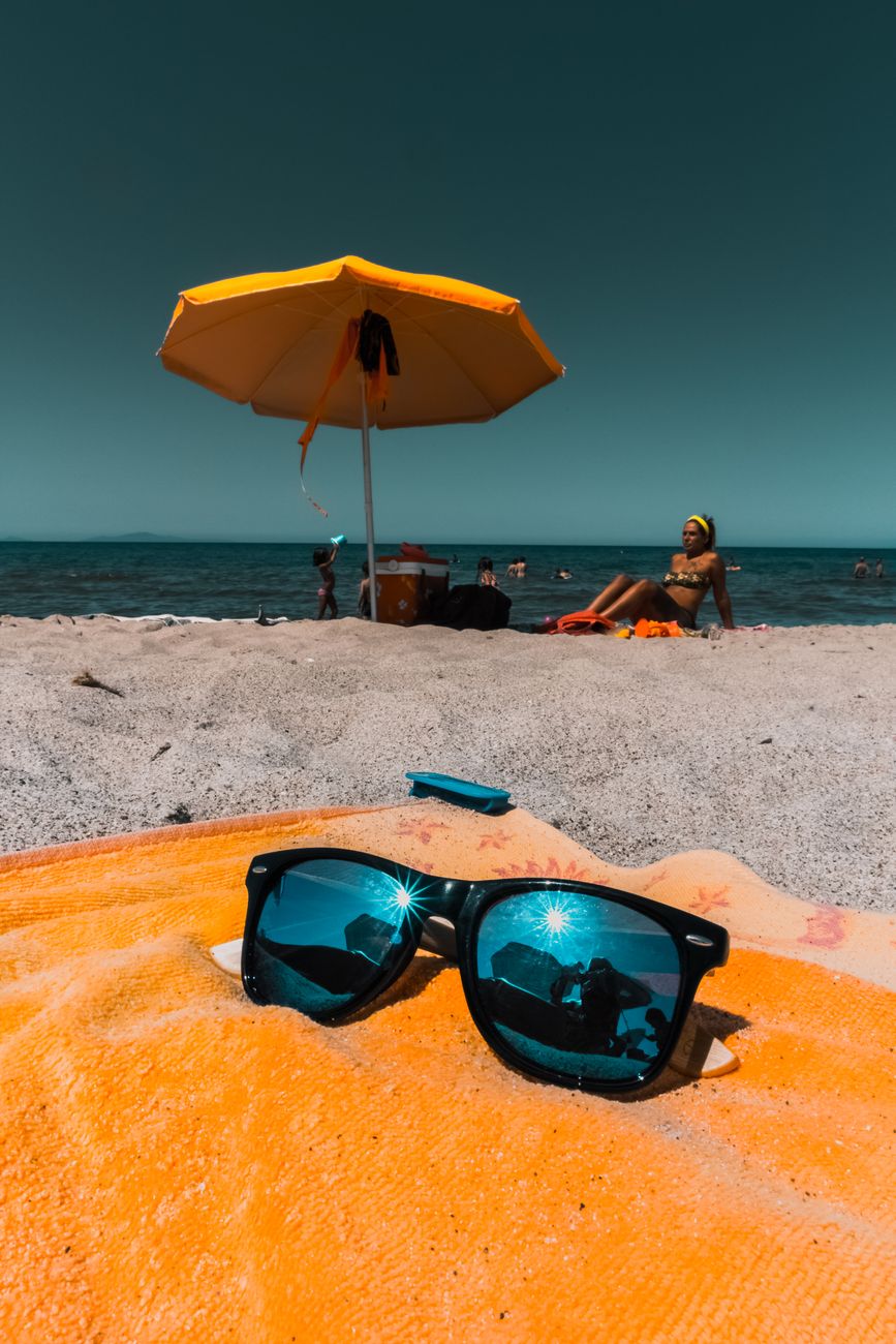 Vibrant beach scene with sunglasses on a towel, sunny ambiance and people relaxing.