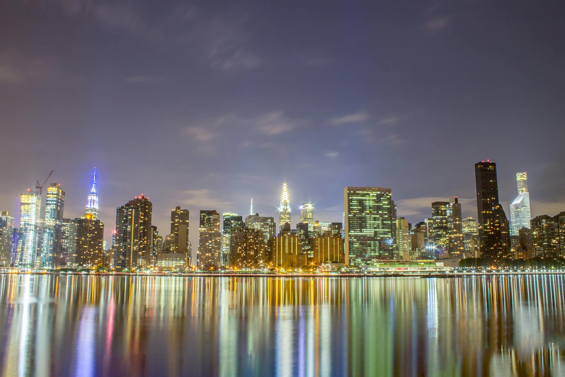 A breathtaking view of the New York City skyline illuminated at night, reflecting in the river.