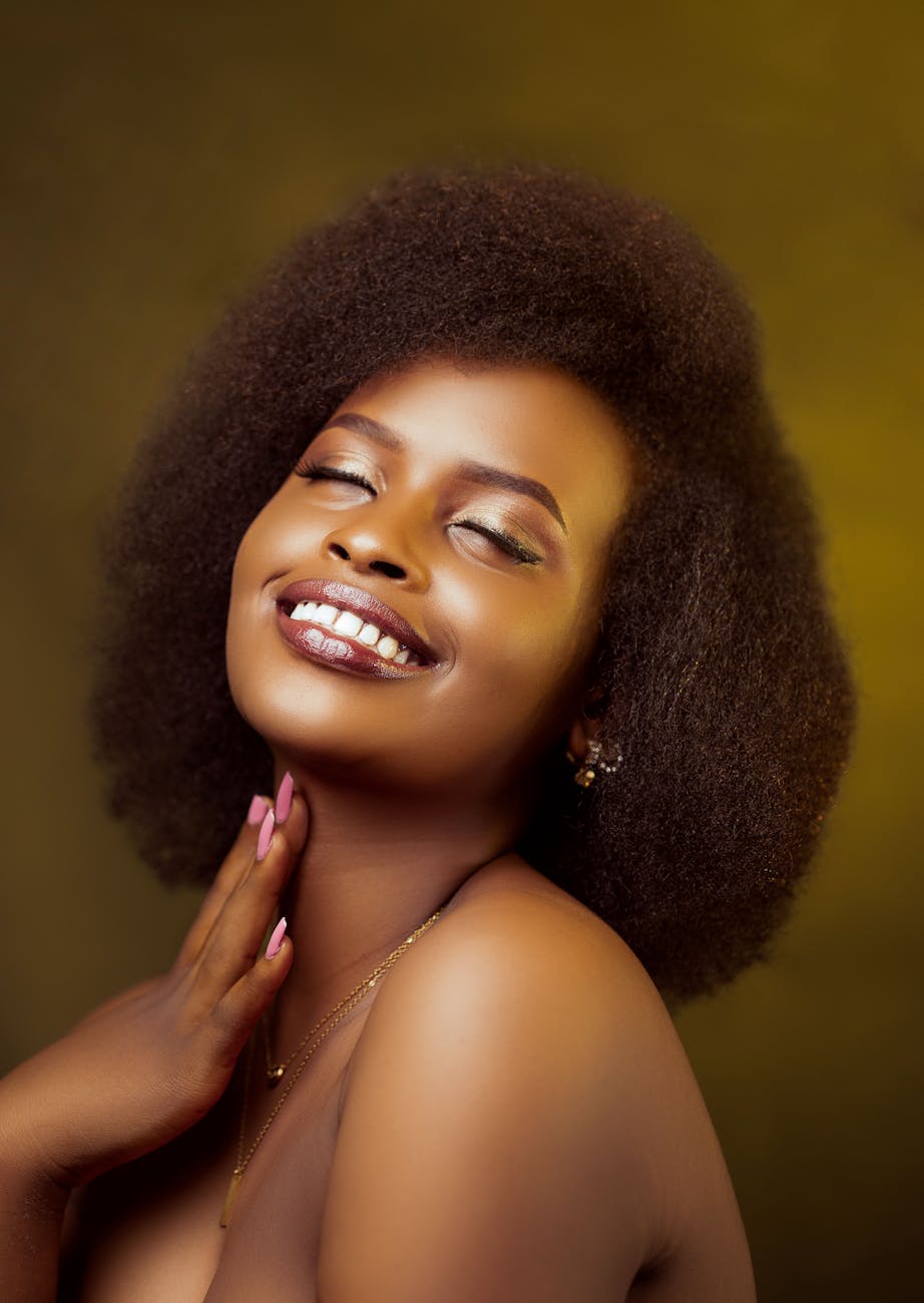 Close-up portrait of a smiling woman with afro hair and elegant makeup.