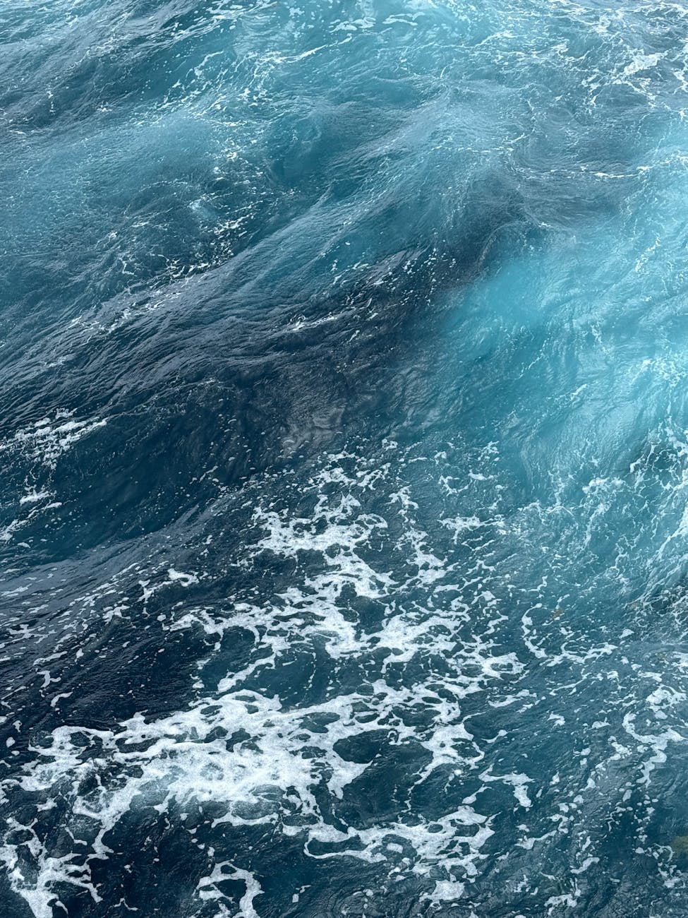 Dynamic view of vibrant ocean waves with frothy white crests in deep blue water.