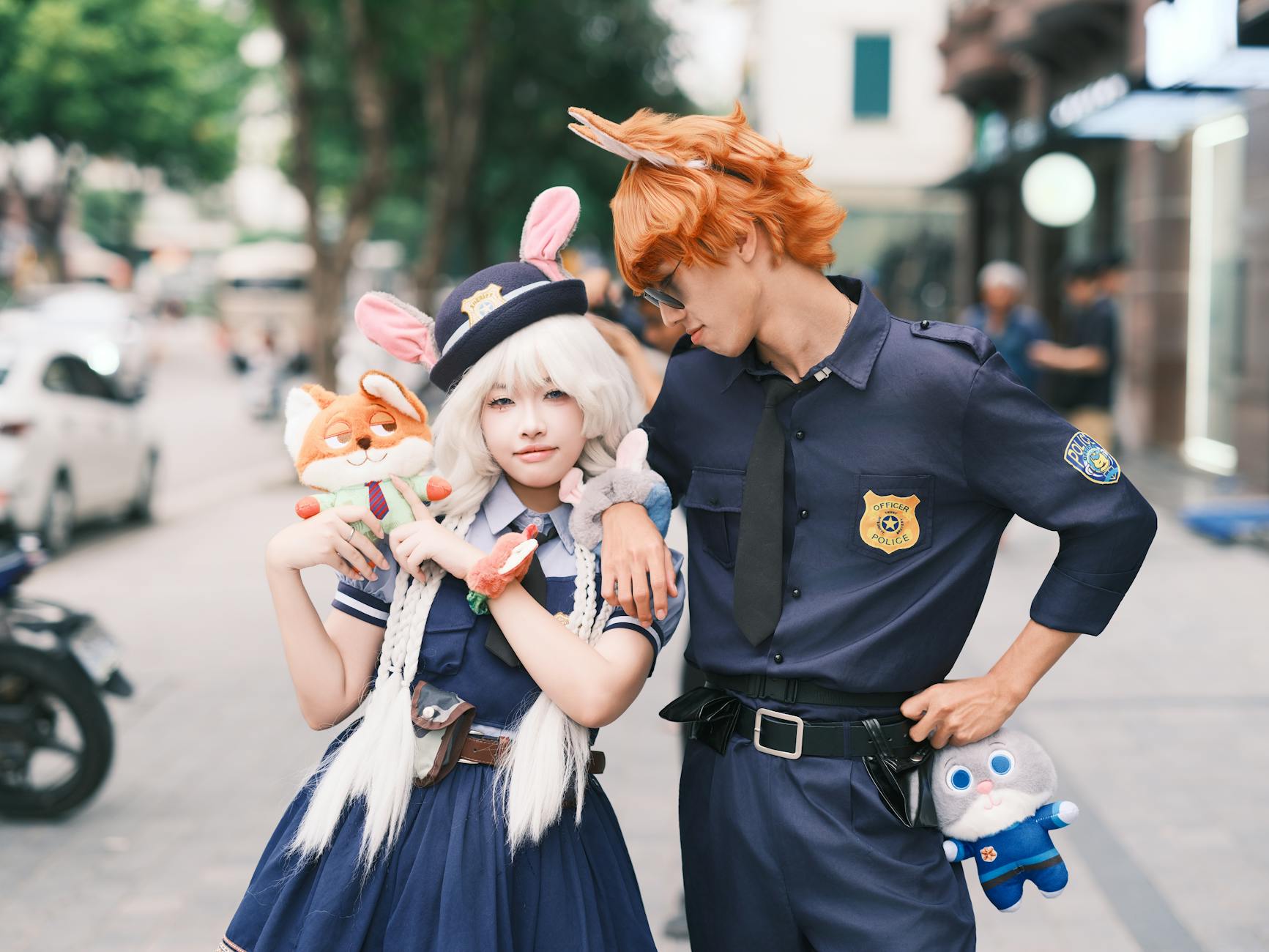Cosplay couple dressed as animal characters from a popular Disney movie, posing outdoors with plush toys.