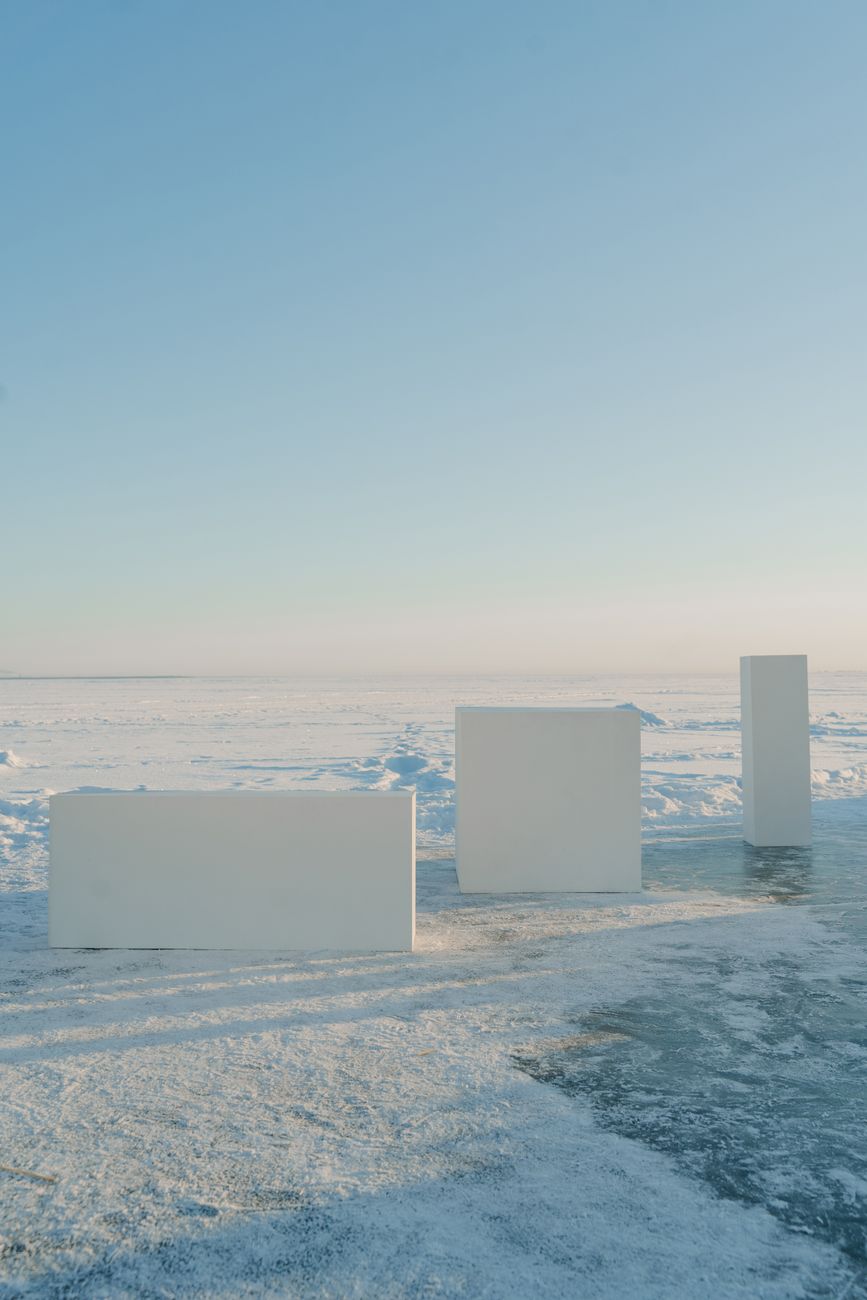 A serene winter landscape featuring minimalist white blocks on a snow-covered ground under a clear blue sky.