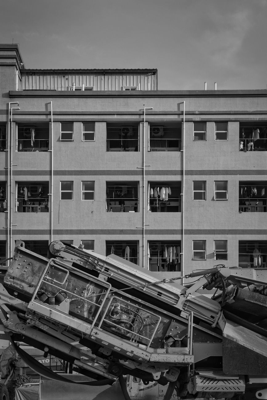 Black and white photo of a construction machine in front of an apartment building.