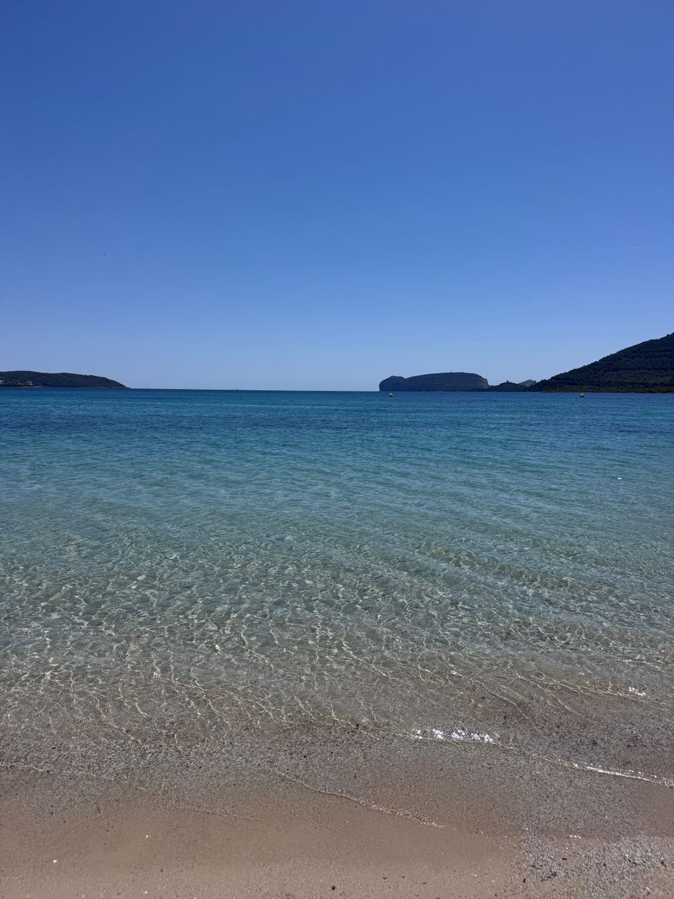 Experience the serene beauty of a Sardinian beach with clear azure waters under a bright summer sky.