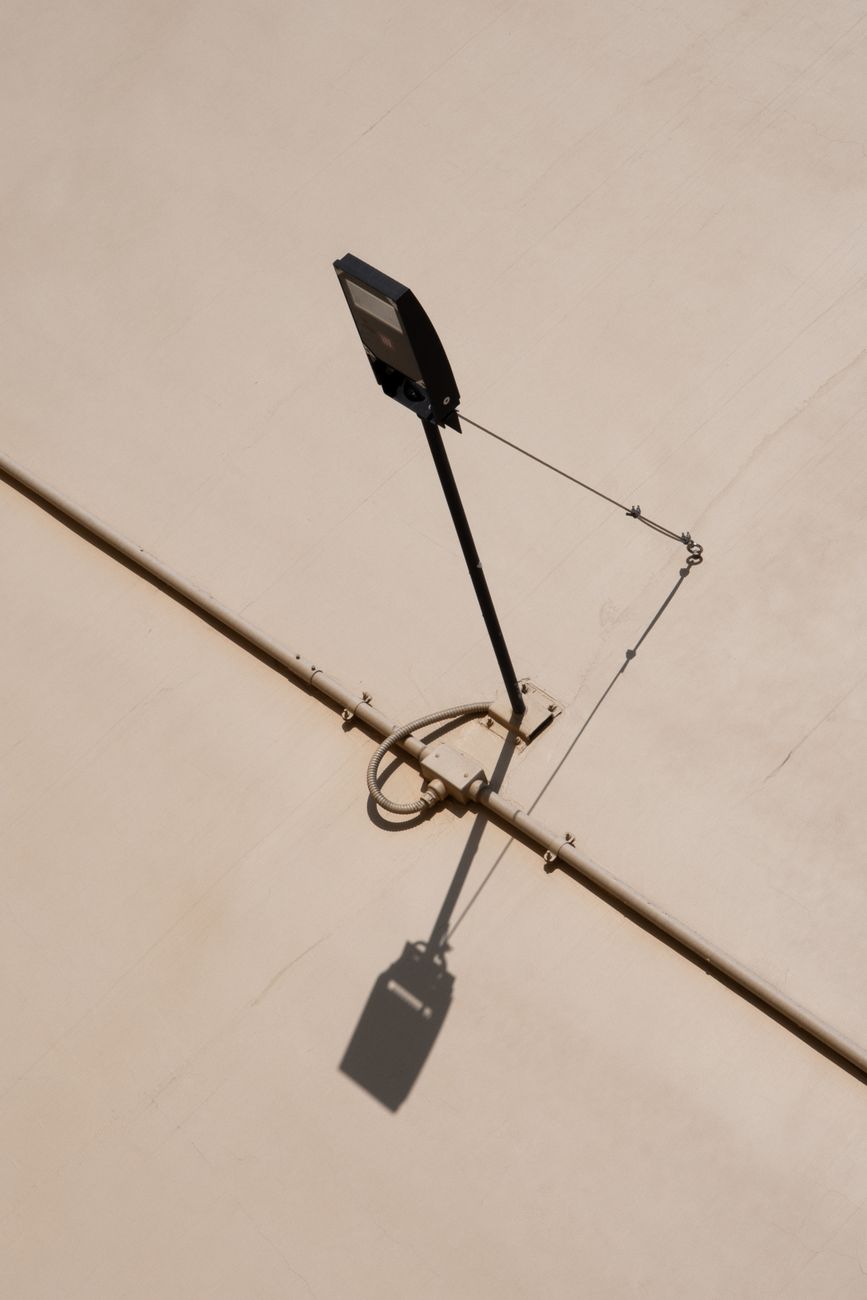 A minimalist street light casting a shadow on a plain beige wall, captured from above.