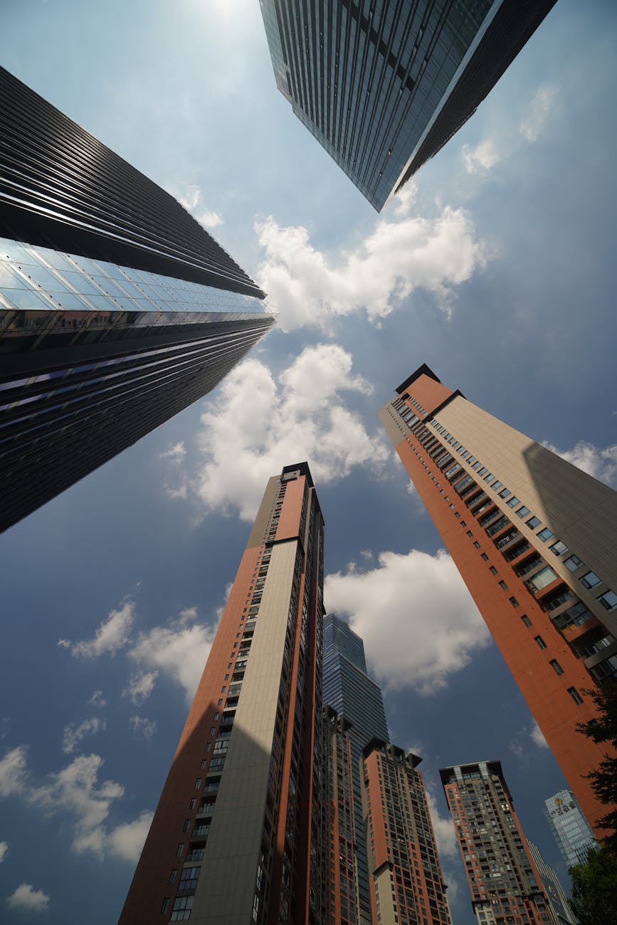 Looking up at tall skyscrapers contrasting with a bright cloudy sky, emphasizing urban architecture.