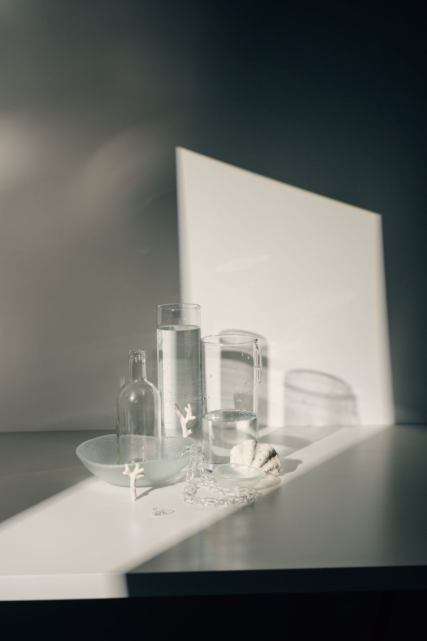 Serene still life of glass bottles, shadows, and objects on a white table reflecting minimalism.