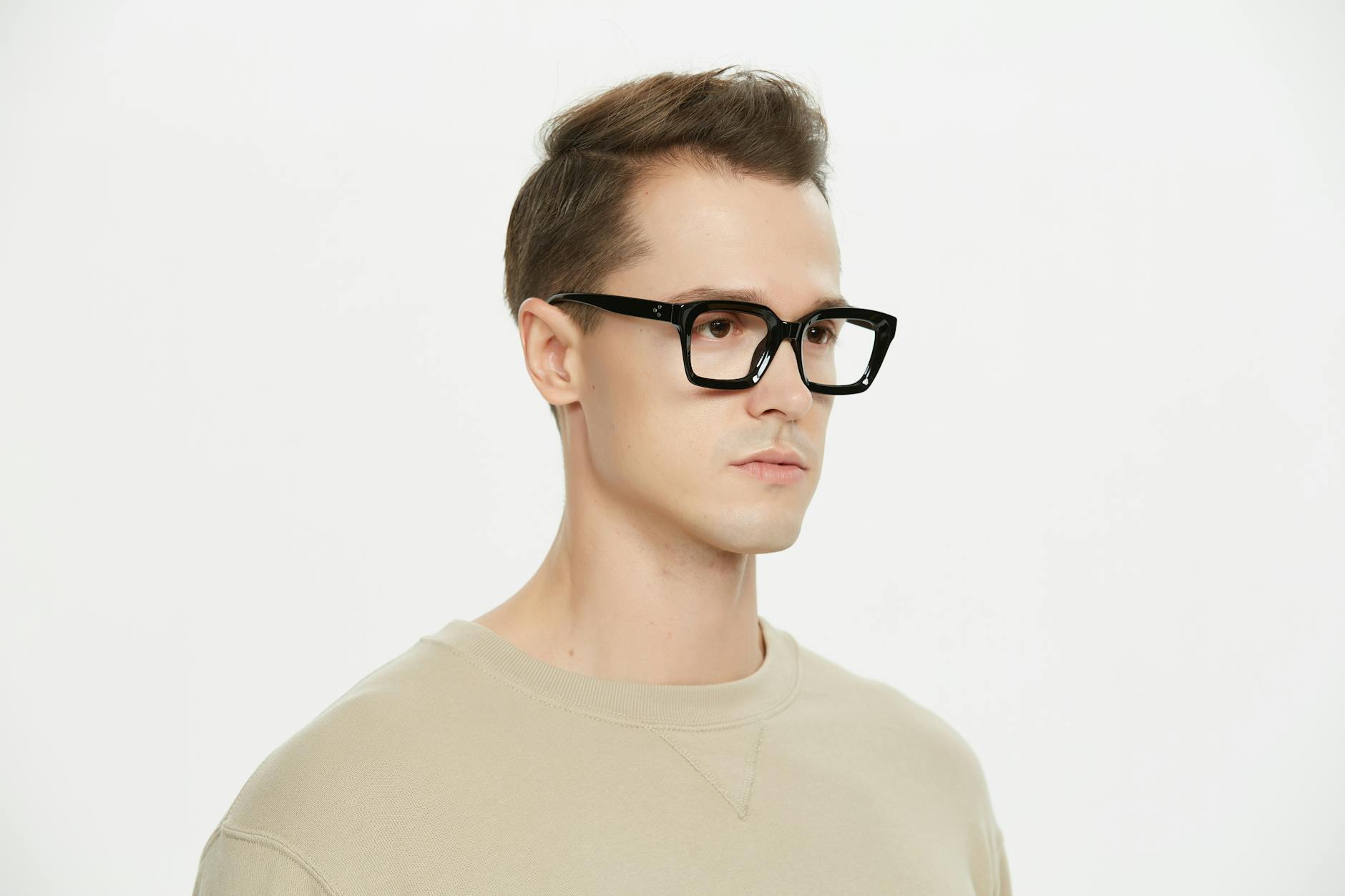 Portrait of a young man wearing black glasses, showcasing modern fashion in a studio setting.