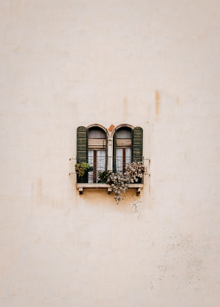 A vintage arched window with green shutters featuring plants, embodying minimalism in architecture.