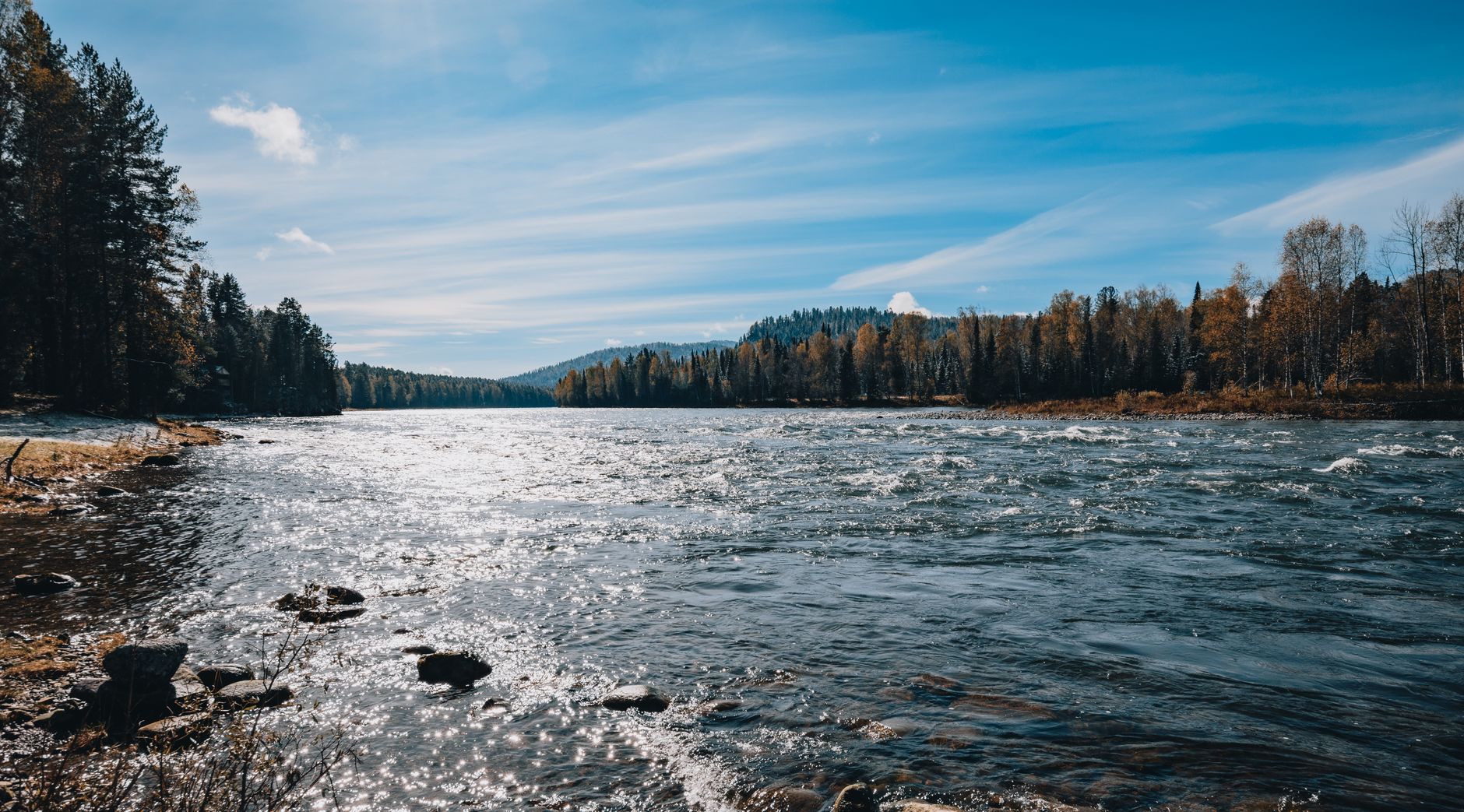 A beautiful river with sparkling water, set against an autumn forest under a clear blue sky.