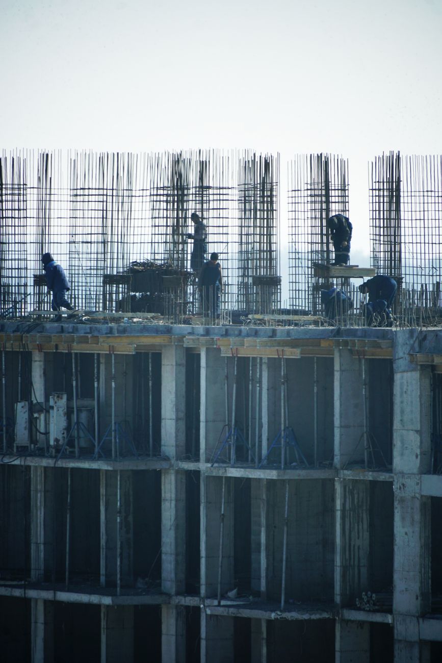 Construction workers at a high-rise building site with visible steel reinforcements.