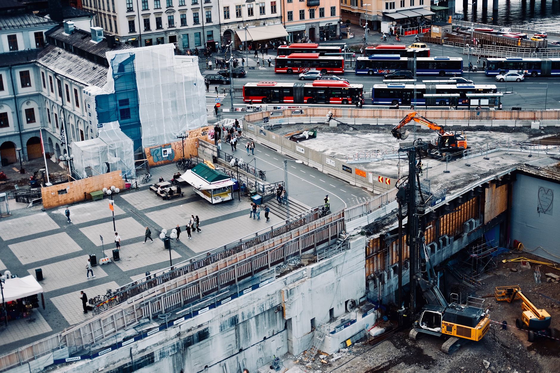 Aerial view of urban construction site in Norrmalm with buses and pedestrians, showcasing city life.