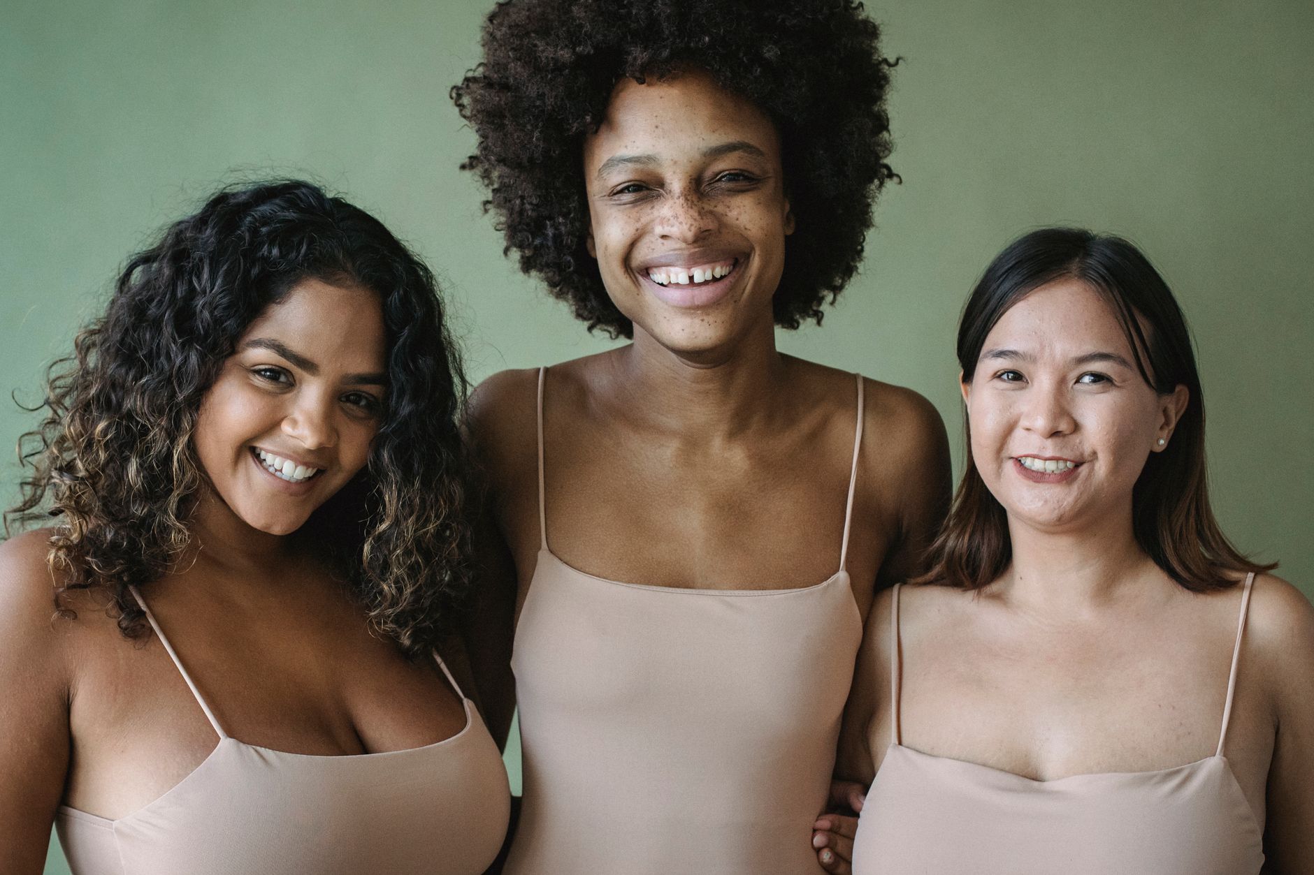Three diverse women smiling in a studio shot, emphasizing beauty and friendship.