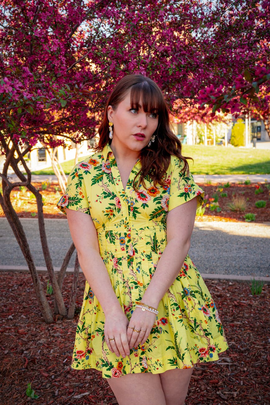 A woman in a vibrant yellow floral dress posing under blooming trees in spring.