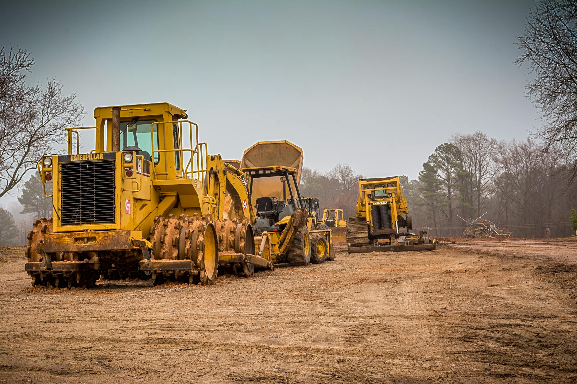 Yellow construction vehicles at a worksite in Raleigh, NC on a cloudy day.
