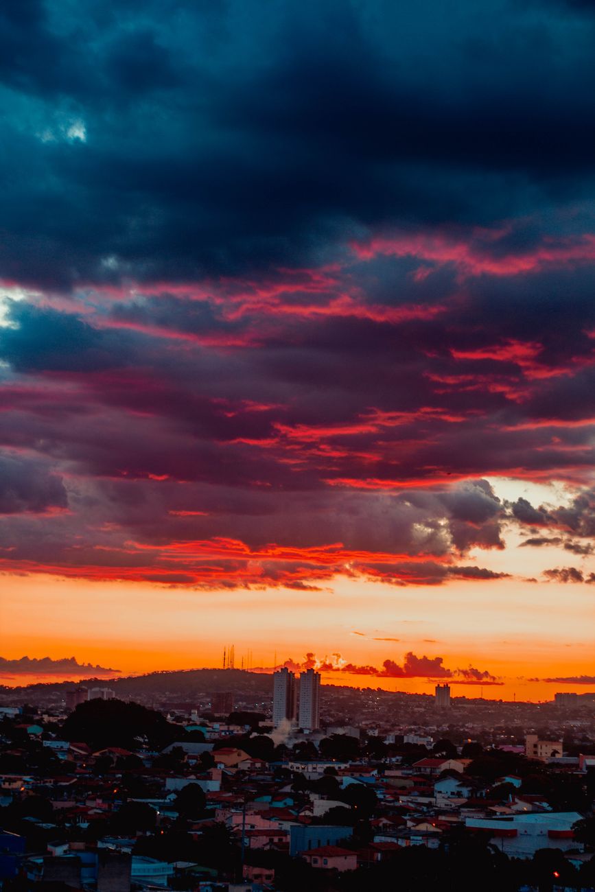Vibrant evening sky covered with dark blue and pink clouds above houses in town and mountain on horizon