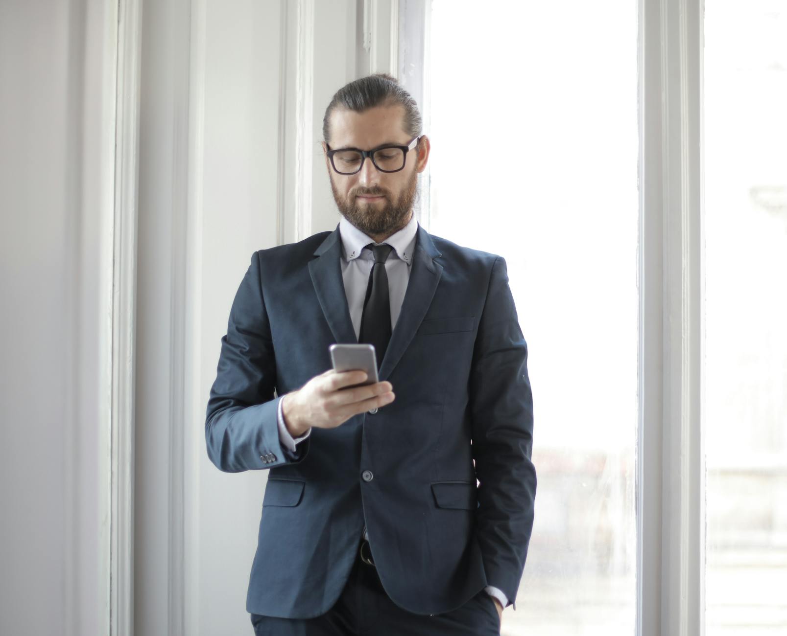 Confident man in formal suit using smartphone by window in office setting.