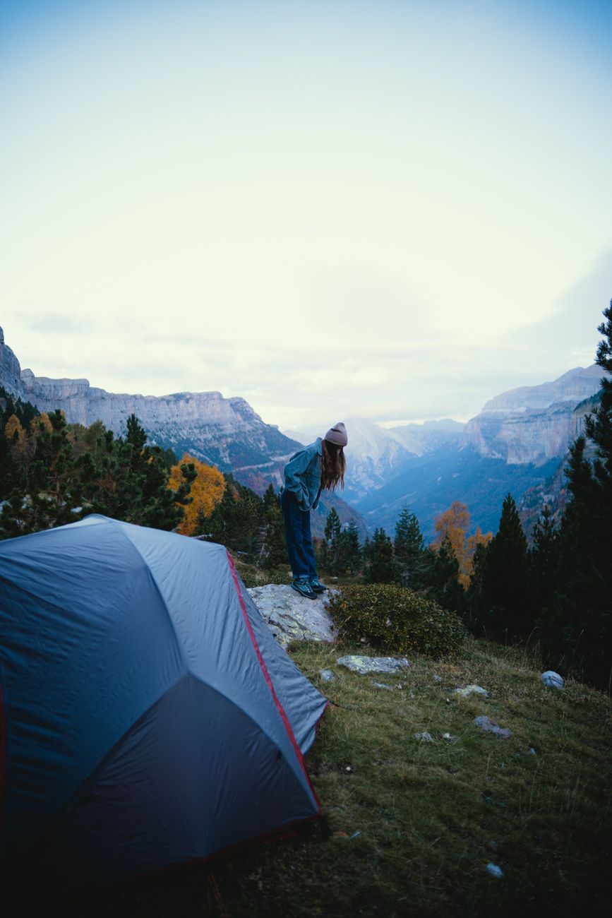 Explore the outdoors with a woman camping in a scenic mountain landscape featuring a tent and lush forest.