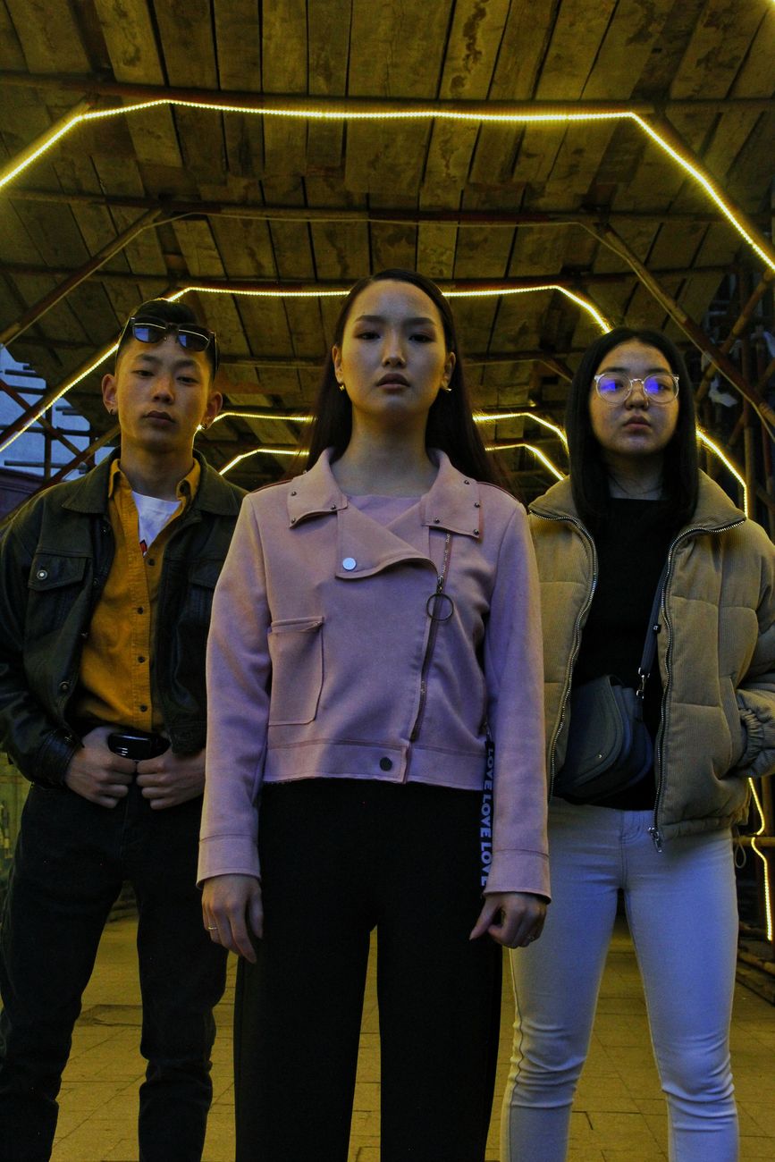 From below of young Asian friends in stylish clothes standing on street under roof with bright illumination
