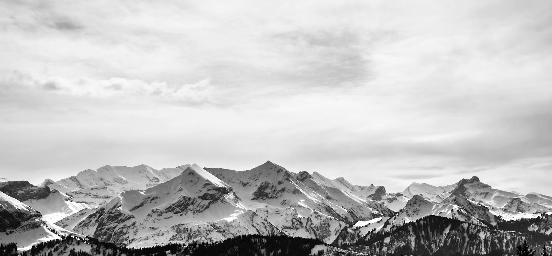 Stunning monochrome landscape of snow-covered alpine mountains under a cloudy sky.