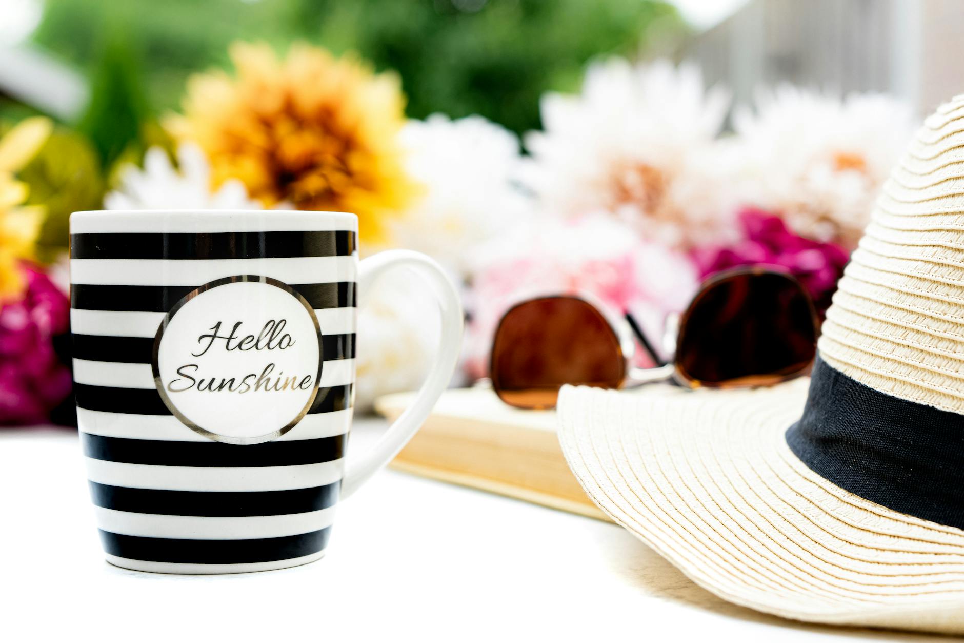 A vibrant summer scene featuring a striped mug, sun hat, and colorful flowers.