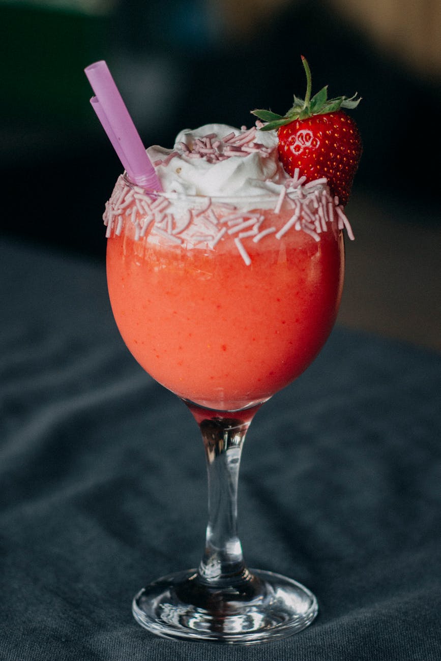 Delicious strawberry smoothie garnished with whipped cream and sprinkles in a wine glass.