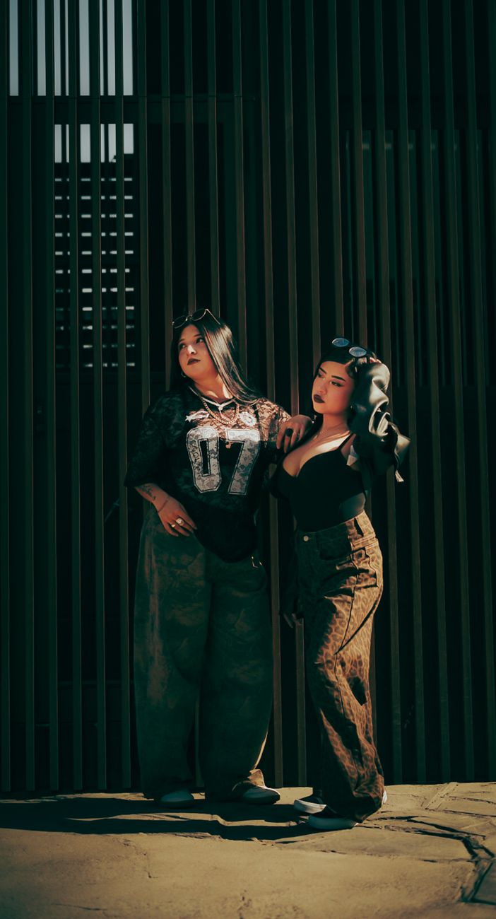 Stylish women pose in front of a slatted wall, showcasing urban fashion.