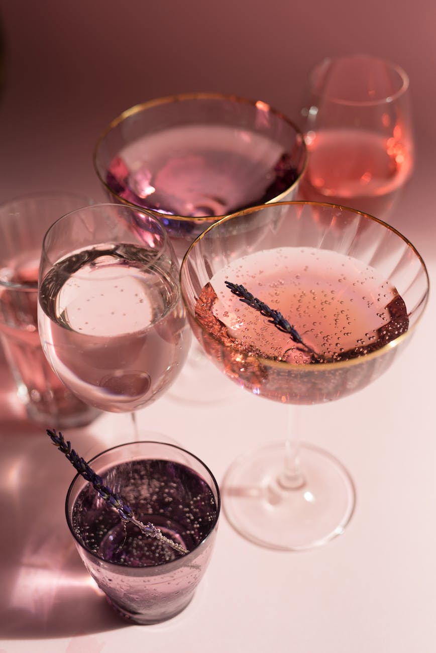 A stylish collection of mixed drinks in elegant glassware on a light pink background.
