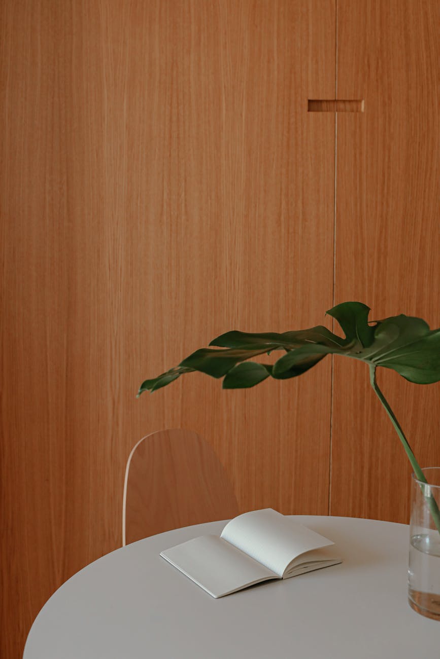 Simple interior featuring a notebook, round table, and leaf in a modern, minimalist style.