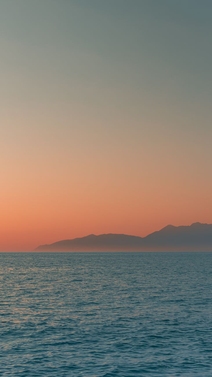 Tranquil sunset view over the serene sea in Corfu, Greece, with distant mountains.