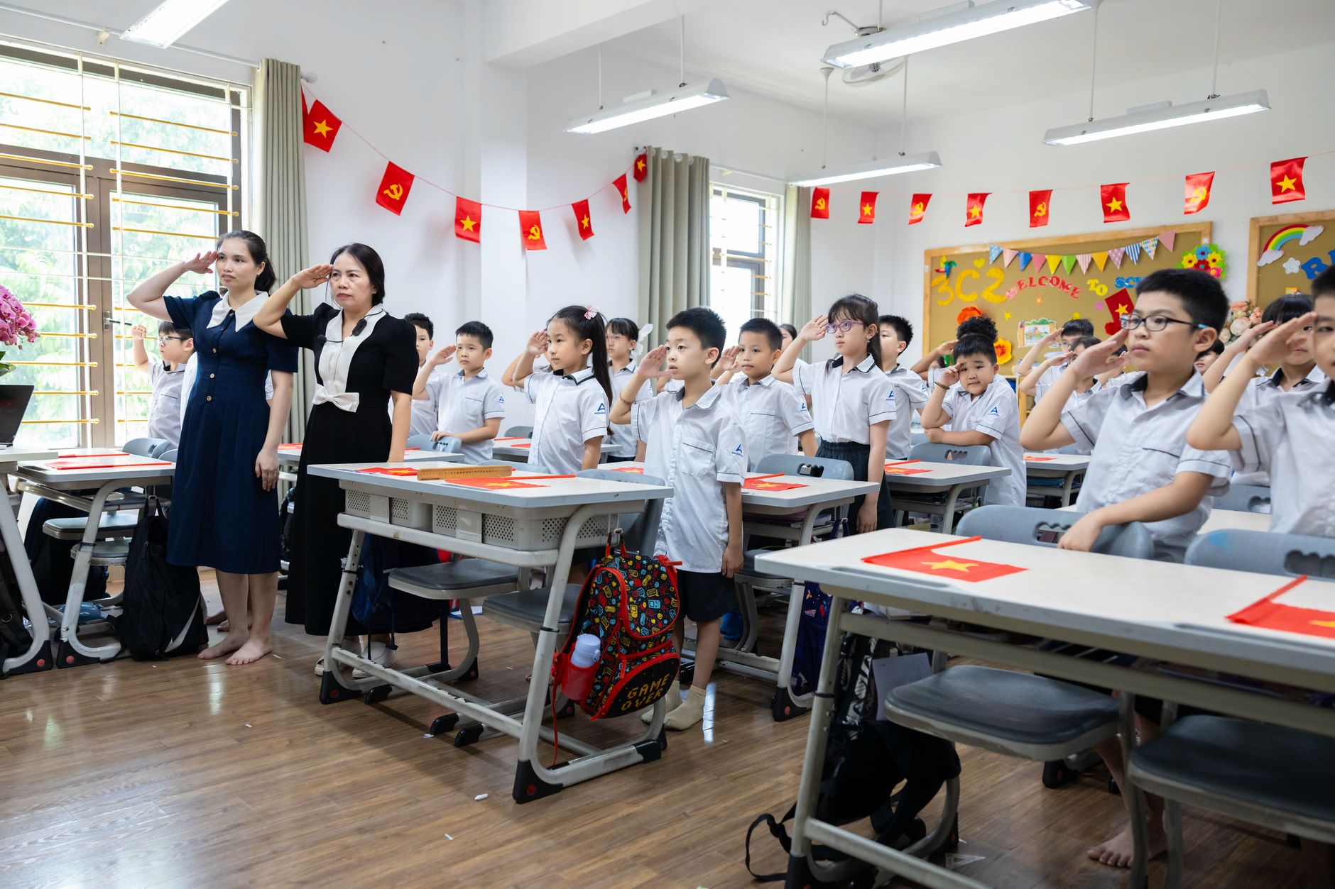 Children and teachers saluting in a colorful classroom decorated with flags.