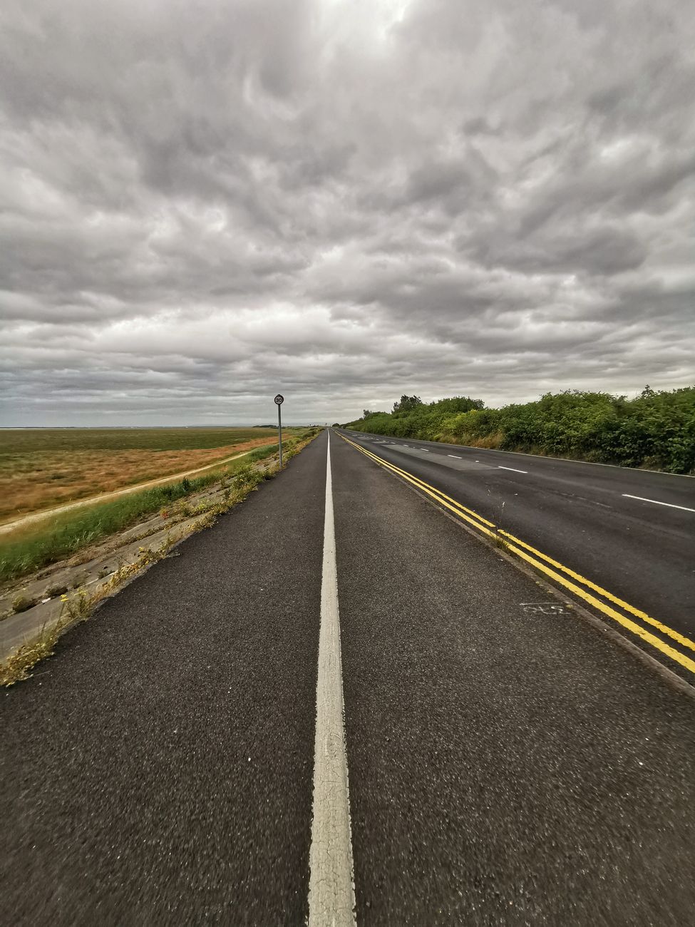 Discover the serene expanse of an empty road under a dramatic, cloudy sky in Merseyside, UK.