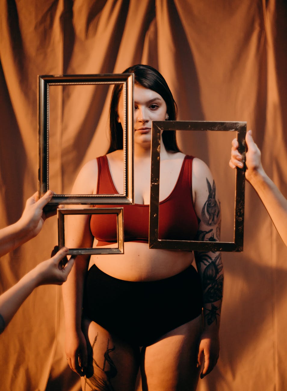 A creative portrait capturing a tattooed plus size woman holding empty frames in a studio setting.