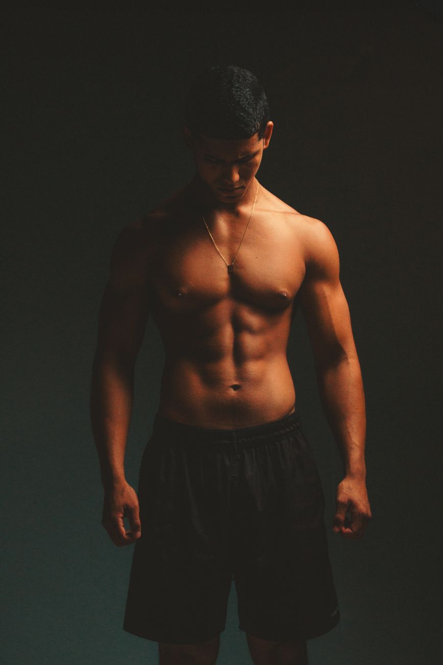 Muscular male athlete posing shirtless in dramatic lighting, showcasing fitness and strength.