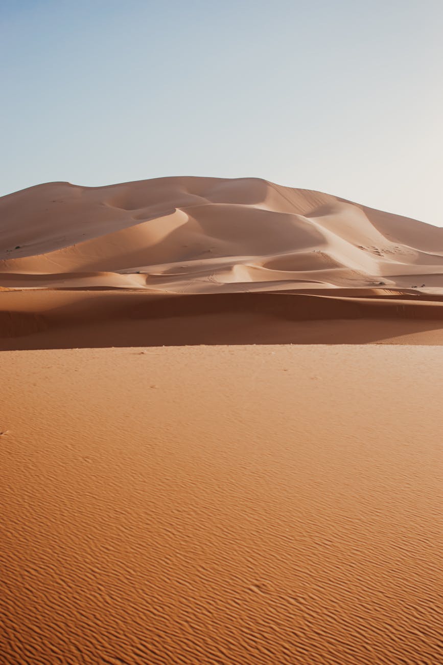 Breathtaking view of the Merzouga desert dunes in Morocco, captured at sunrise showcasing ripples and a vast landscape.