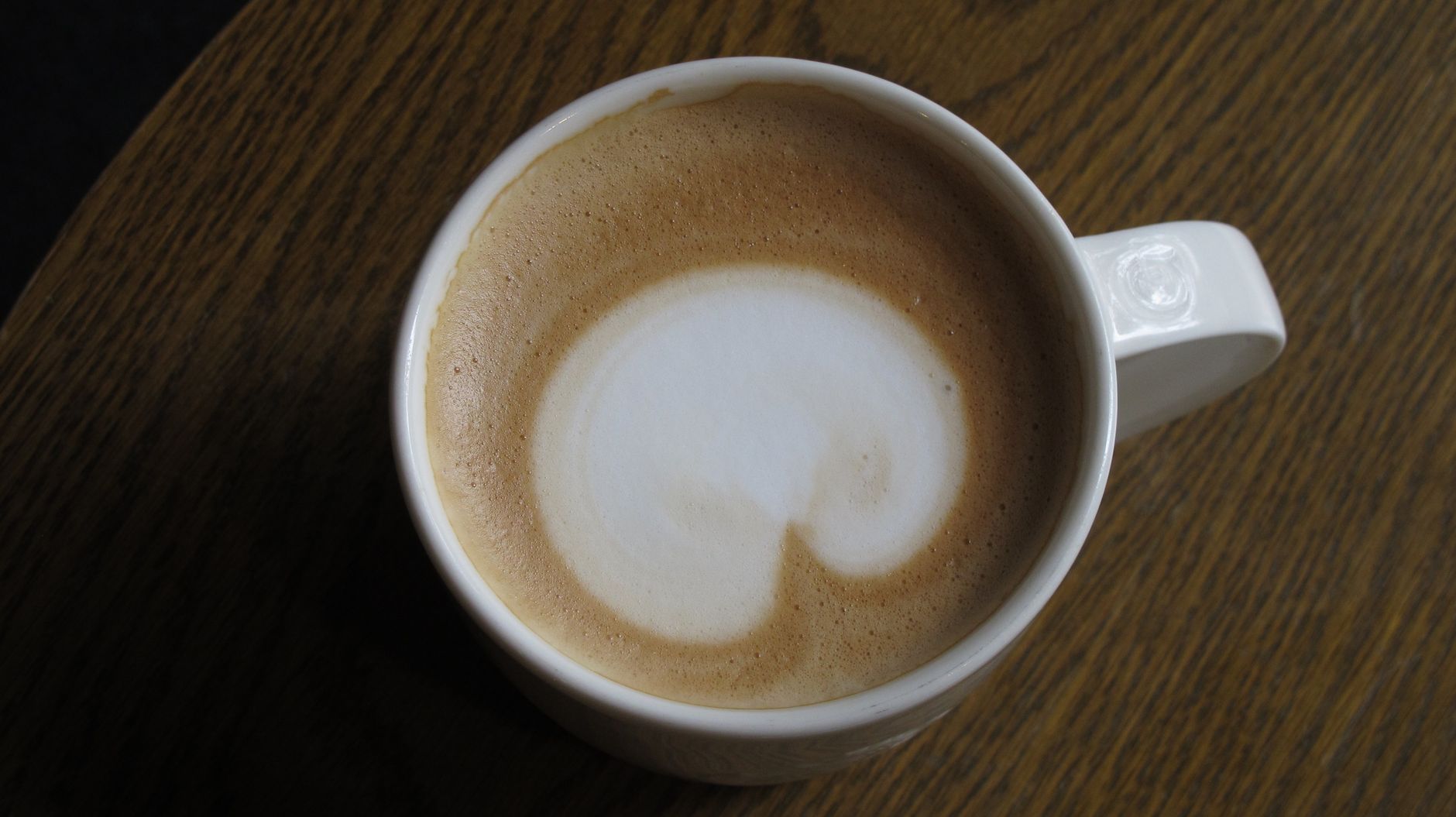 A top view of a frothy cappuccino in a ceramic cup placed on a wooden table.