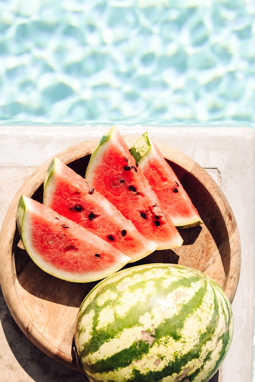 Sliced watermelon on a wooden plate by a pool in Greece, perfect for summer refreshment.