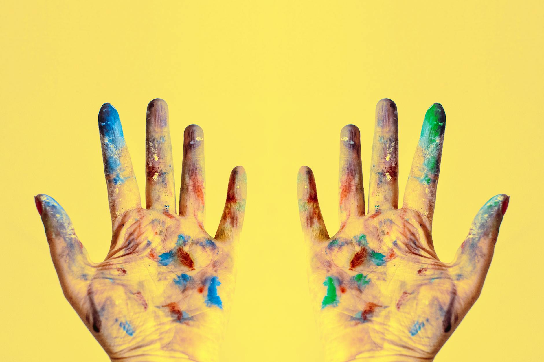 Colorful fingers spread against a bright yellow backdrop, showcasing creativity.